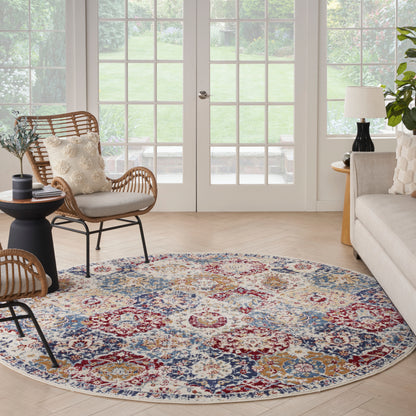 Round floral area rug in blue, red, gold and cream; paired with wicker chairs and a beige sofa in a bright living room.