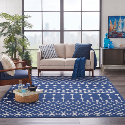 Navy geometric rug in a coastal living room with a beige sofa, blue pillows, wicker coffee tray, and large windows.