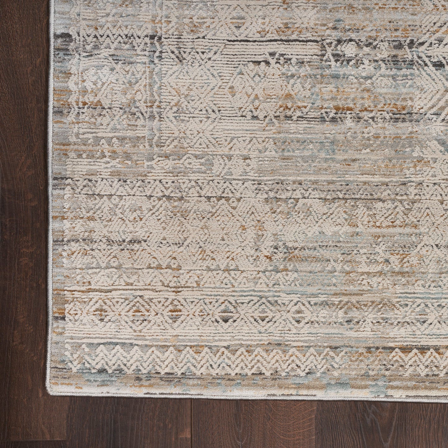Distressed geometric area rug in beige, blue and taupe on dark hardwood floor.