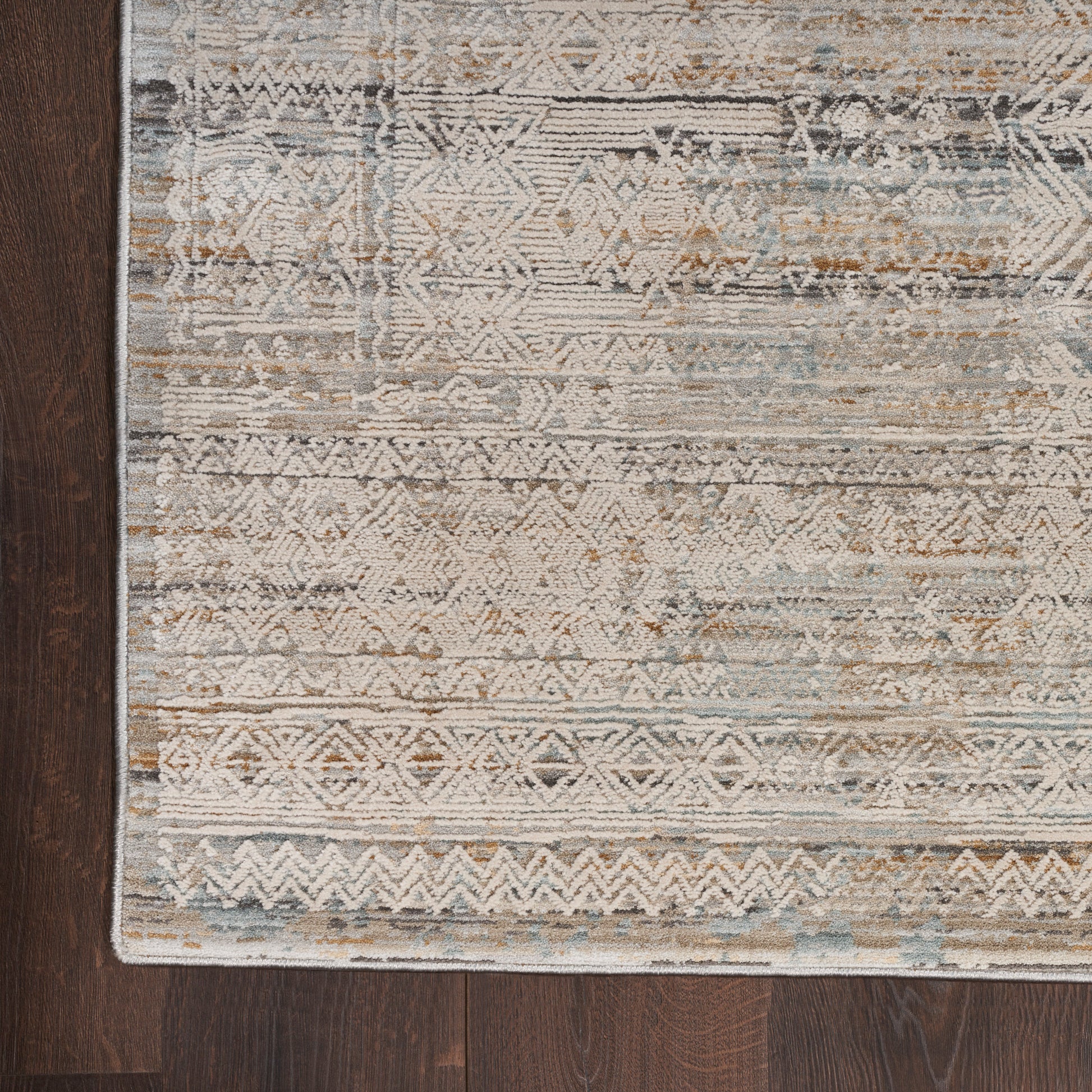 Distressed geometric area rug in beige, blue and taupe on dark hardwood floor.