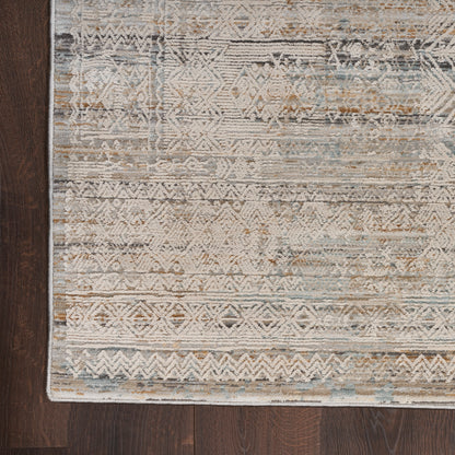 Distressed geometric area rug in beige, blue and taupe on dark hardwood floor.