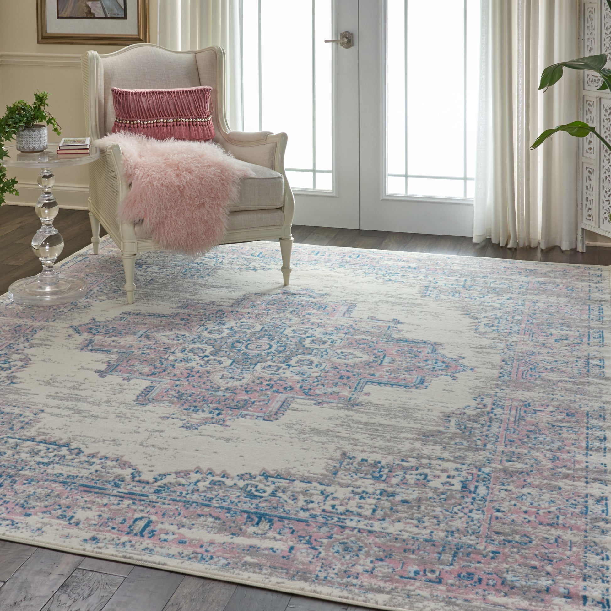 Cream wingback chair with pink pillow and fluffy pink throw, beside glass side table on a pastel pink-blue vintage rug.
