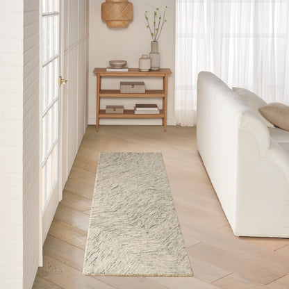 Minimalist light-wood hallway console with shelves, gray textured runner rug, white sofa and sheer curtains.