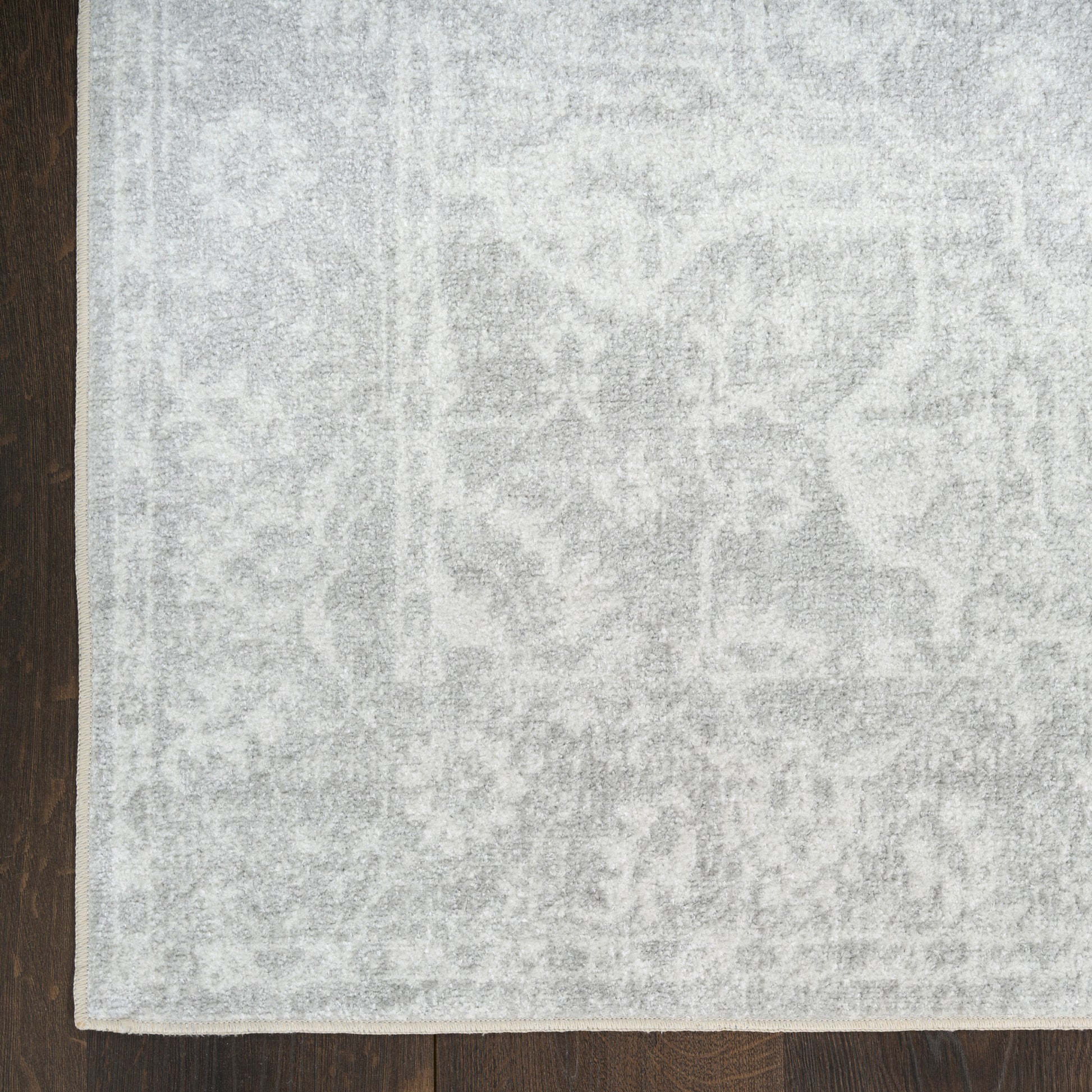 Rectangular light gray area rug with a subtle medallion pattern on a dark wood floor.