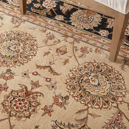 Beige traditional floral area rug with large medallions and blue accents; chair leg visible.