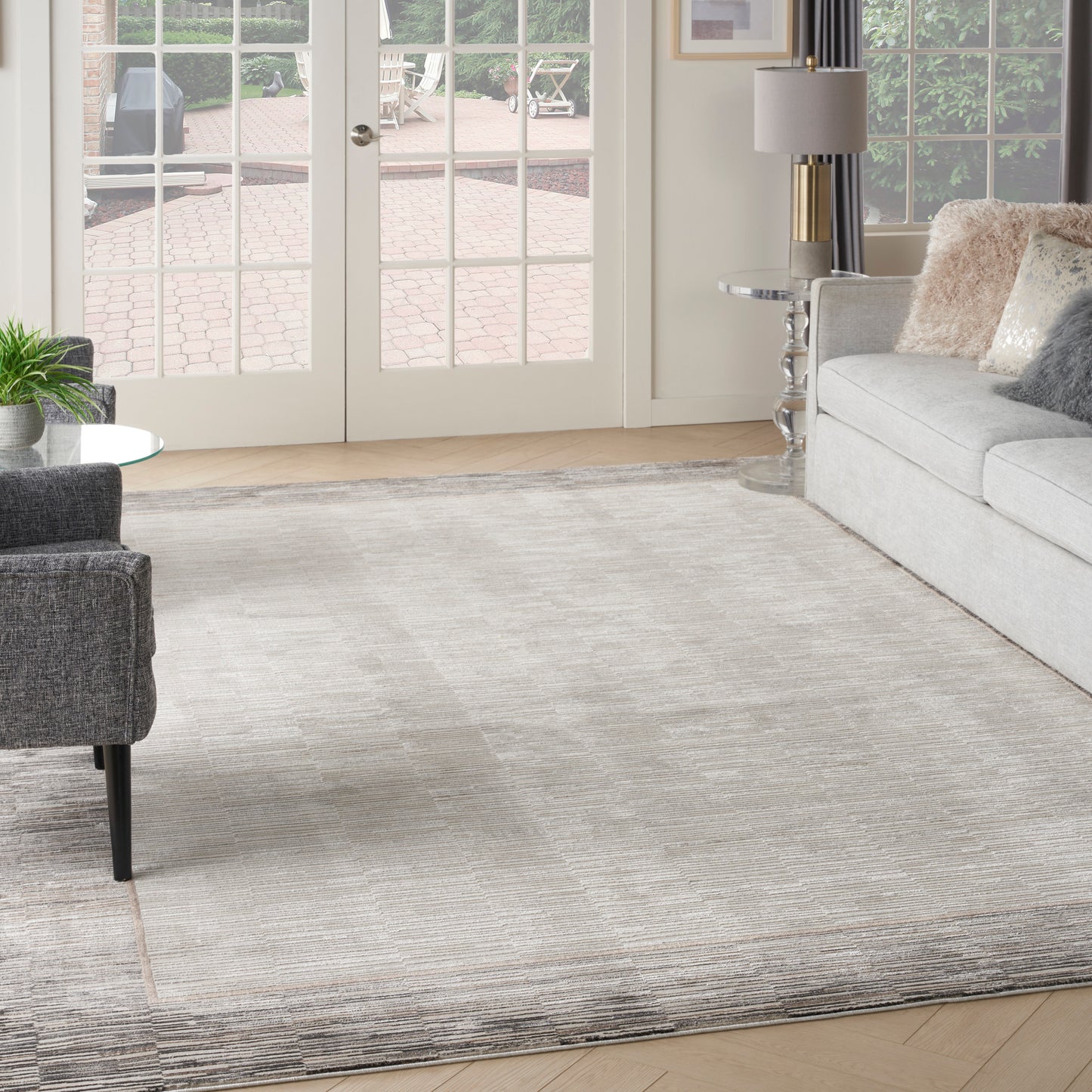Neutral gray textured area rug in a modern living room with gray sofa, dark armchair, glass side table, and French doors.