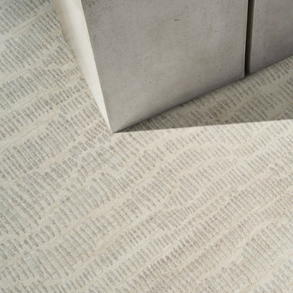 Beige textured rug with a subtle geometric weave, shown near light gray concrete blocks.