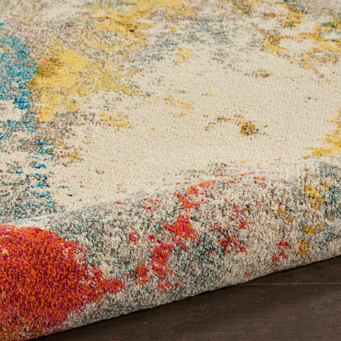 Close-up of a plush rug with cream base & bright teal, yellow, pink accents; thick pile & rolled edge.