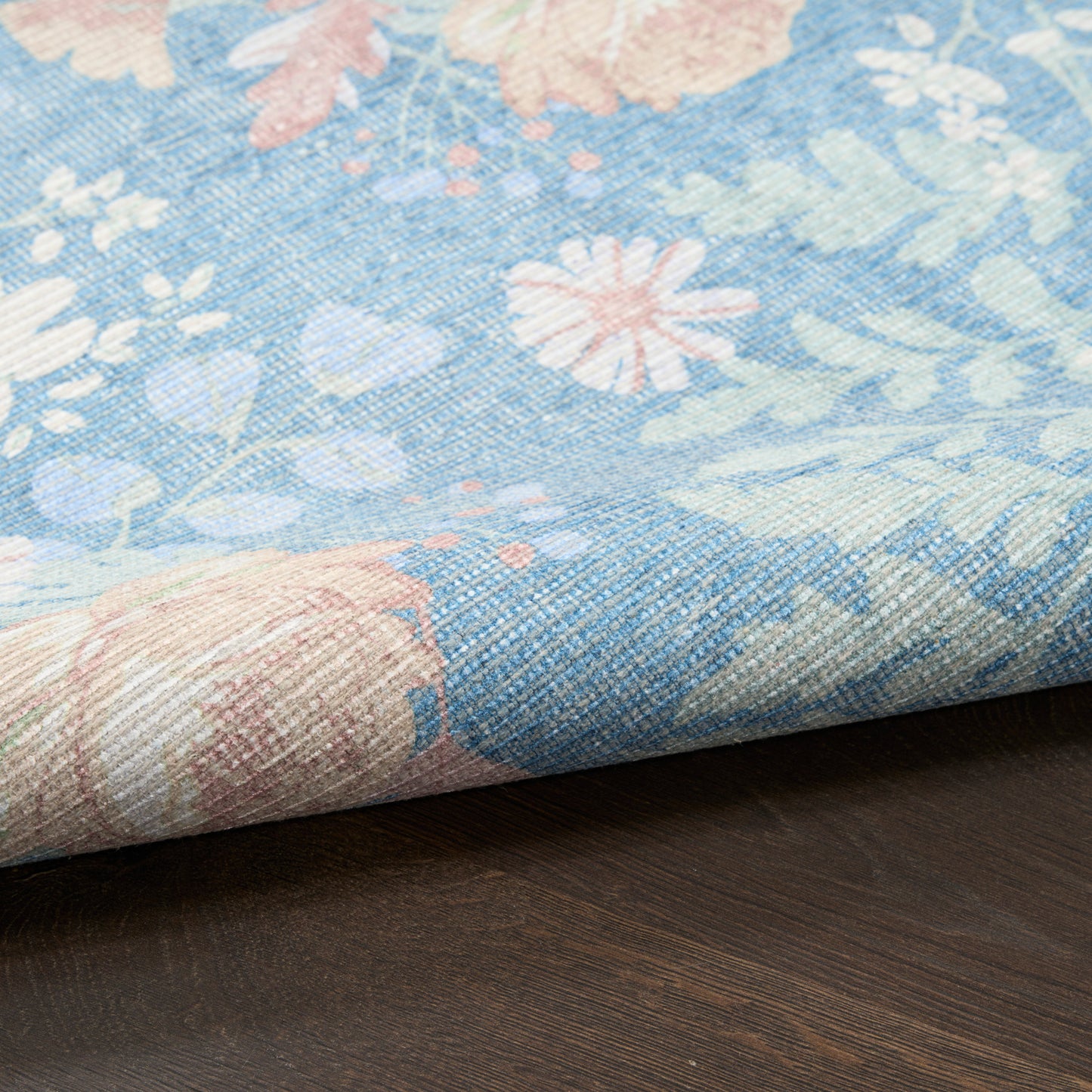 Pastel blue floral-printed woven rug with pink and white blossoms, folded on a dark wood surface.