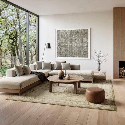 Neutral living room with L-shaped beige sectional, round wooden coffee table, large window view of trees, abstract wall art.