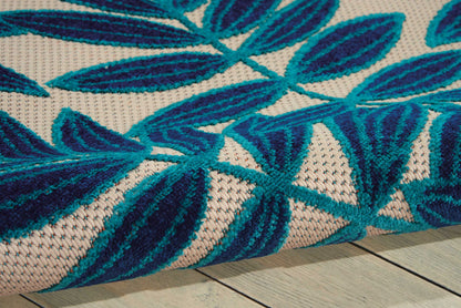 Woven rug with teal blue leaf pattern on natural beige; textured flat-weave, tropical boho style, suitable for living rooms.