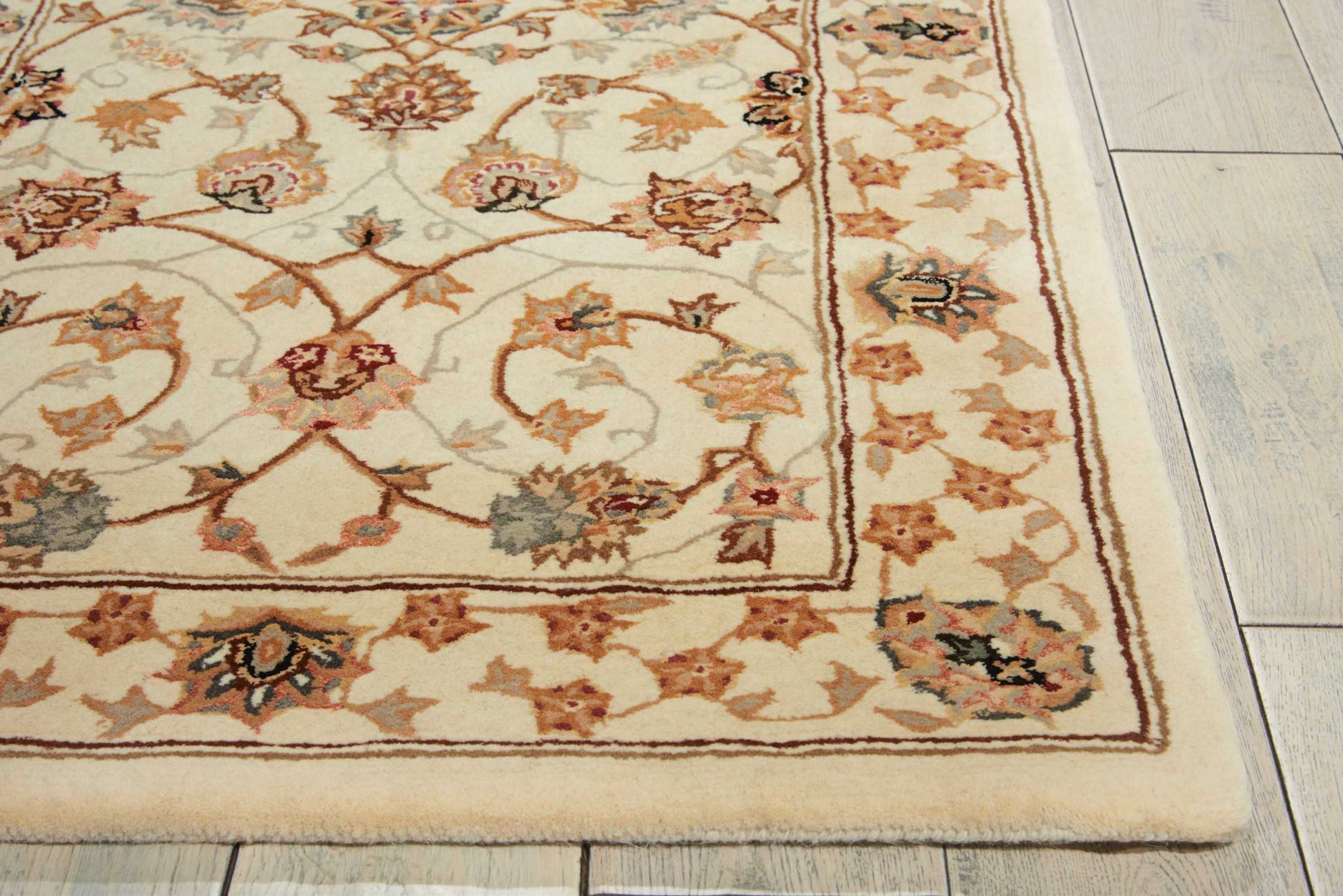 Rectangular cream oriental-style area rug with a floral vine border in tan, red, and blue on a light wood floor.