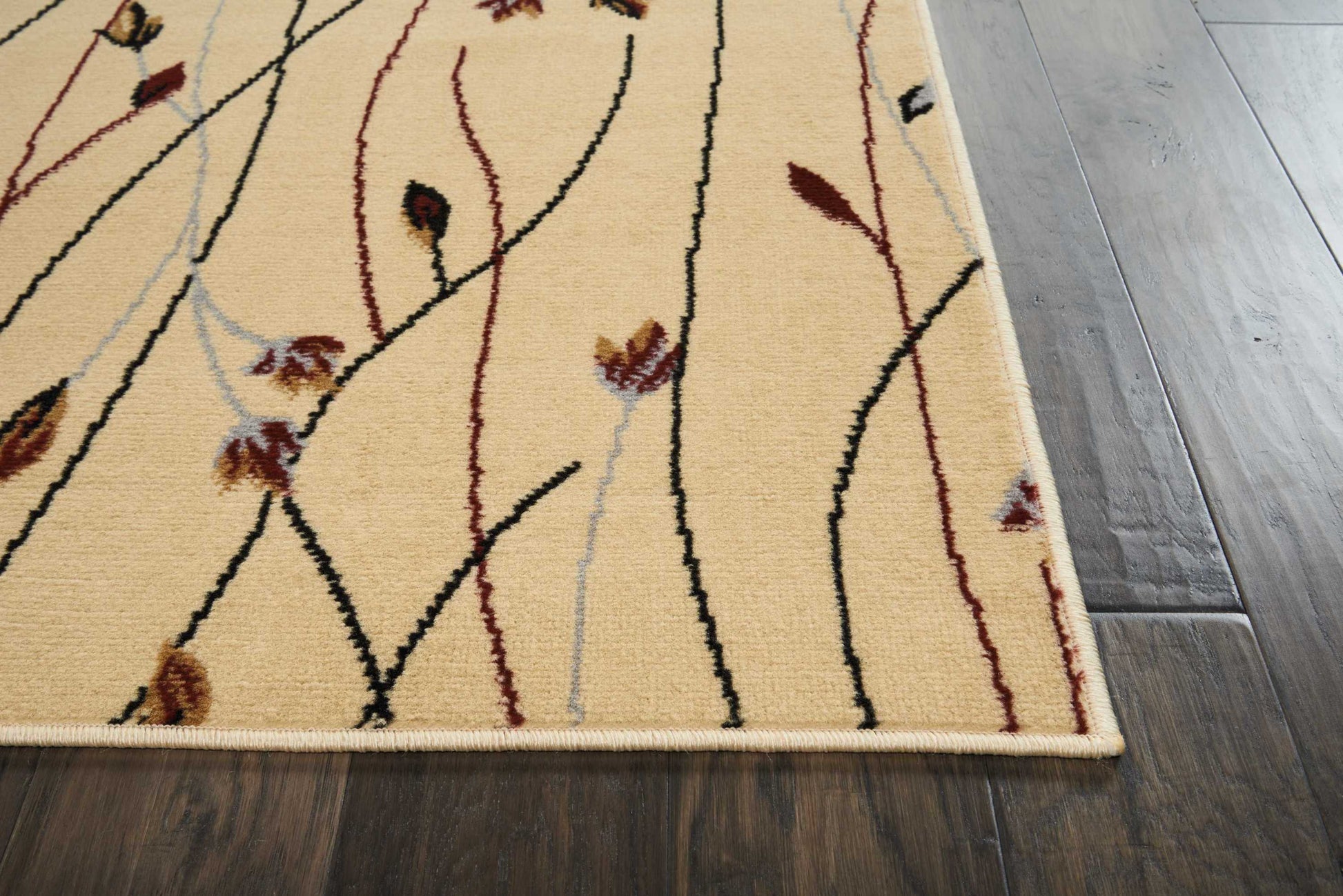 Beige abstract area rug with slender black, red and gray vines and small leaf accents on a dark hardwood floor.