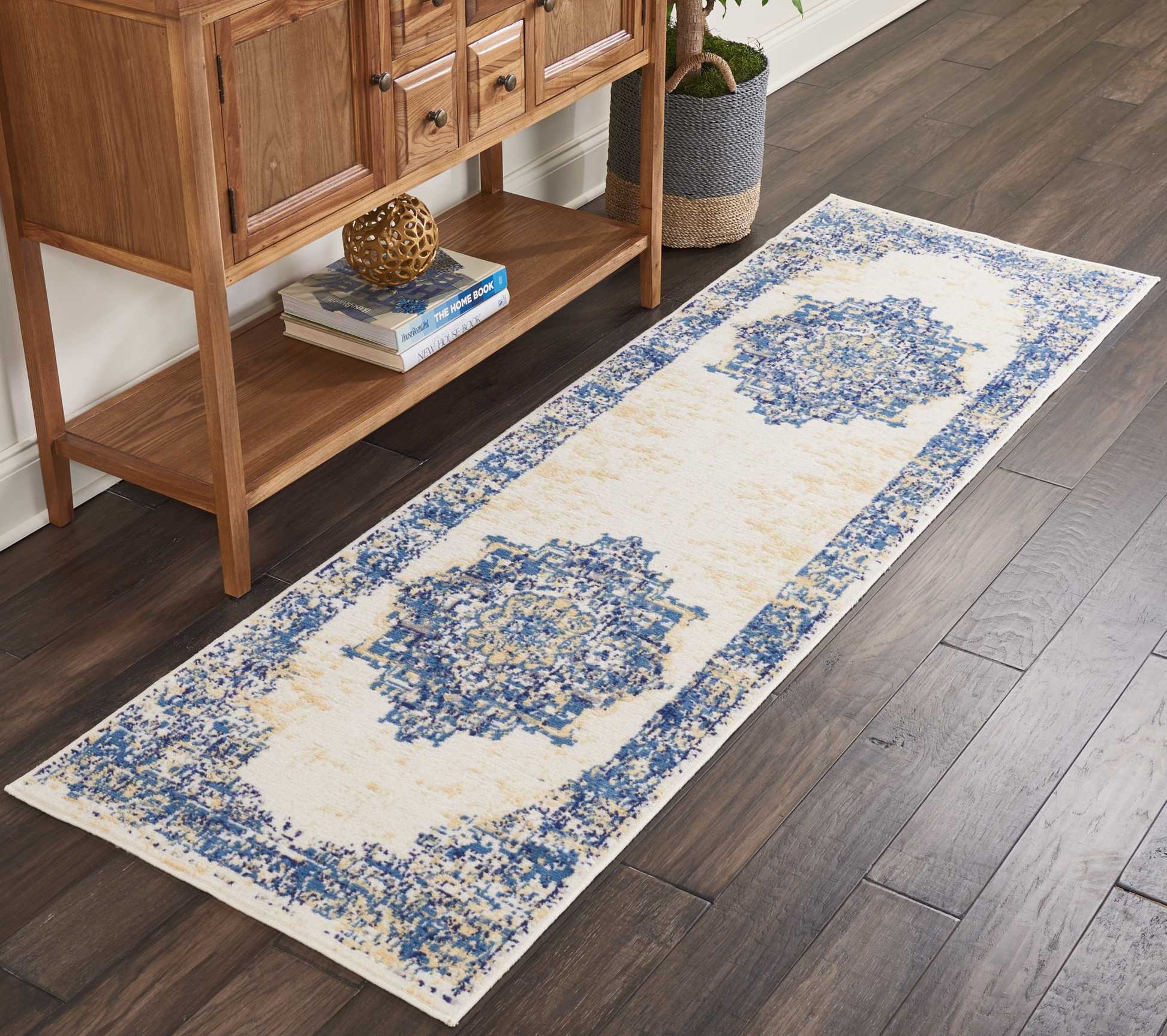 Ivory hall runner rug with blue medallion pattern and blue border, laid along dark wood floor beside a wooden console.