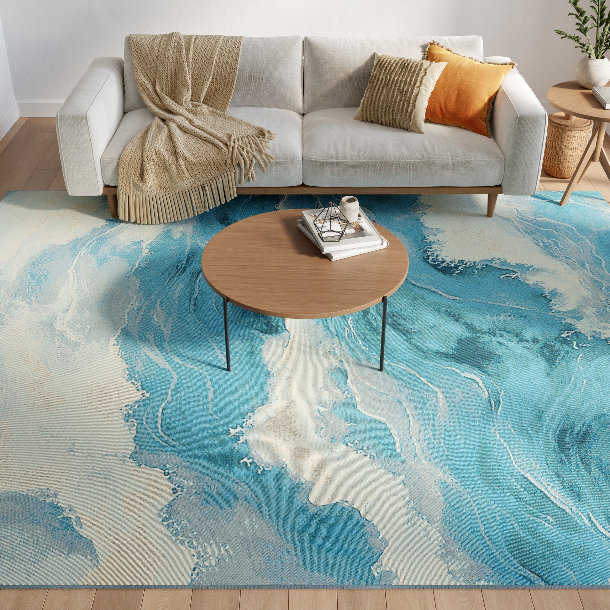 Light gray sofa with beige throw and mustard pillows, round wood coffee table, blue teal abstract rug.