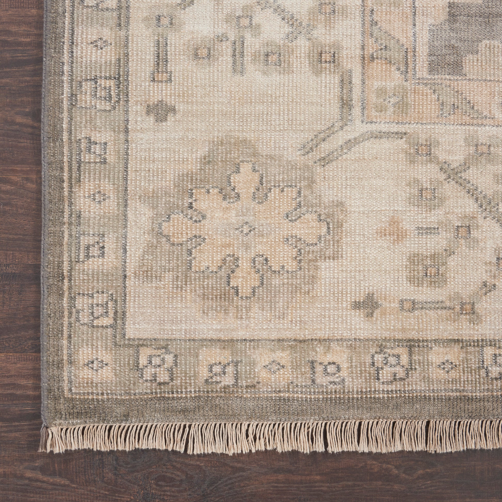 Beige oriental area rug with floralmedallion, muted taupe and ivory palette, fringed border on dark wood floor.