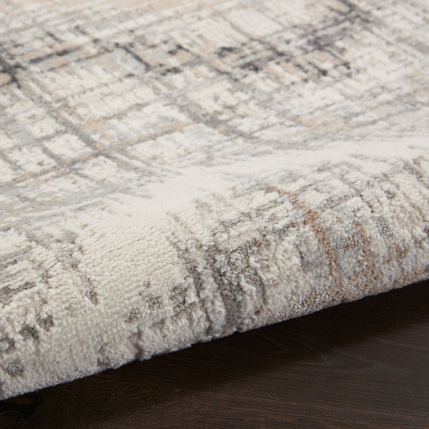 Neutral-toned plush rug with a geometric pattern and folded edge on dark wood floor.