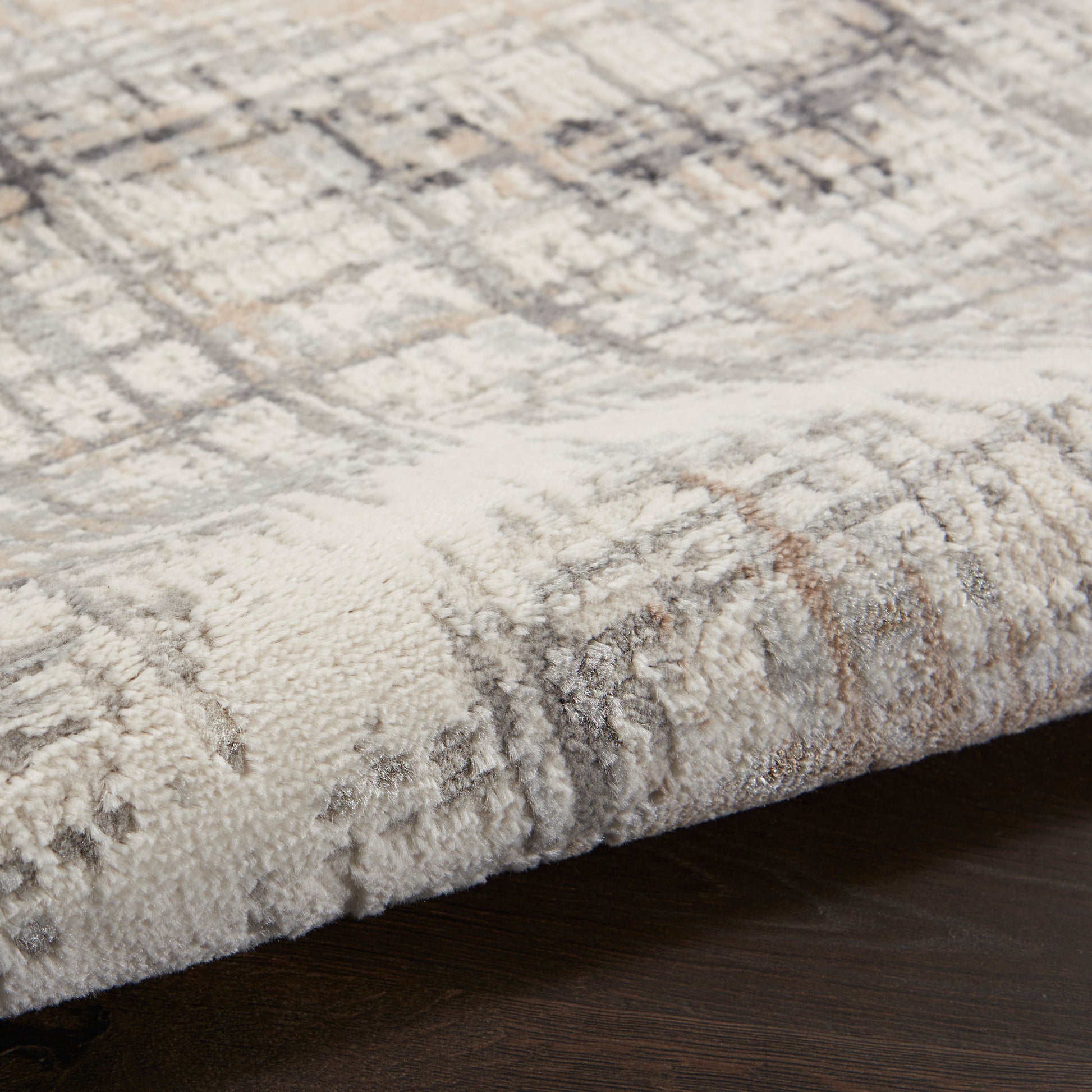 Neutral-toned plush rug with a geometric pattern and folded edge on dark wood floor.