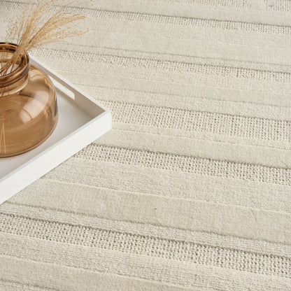 Beige striped rug with a white tray holding an amber glass vase and dried grass sprigs.