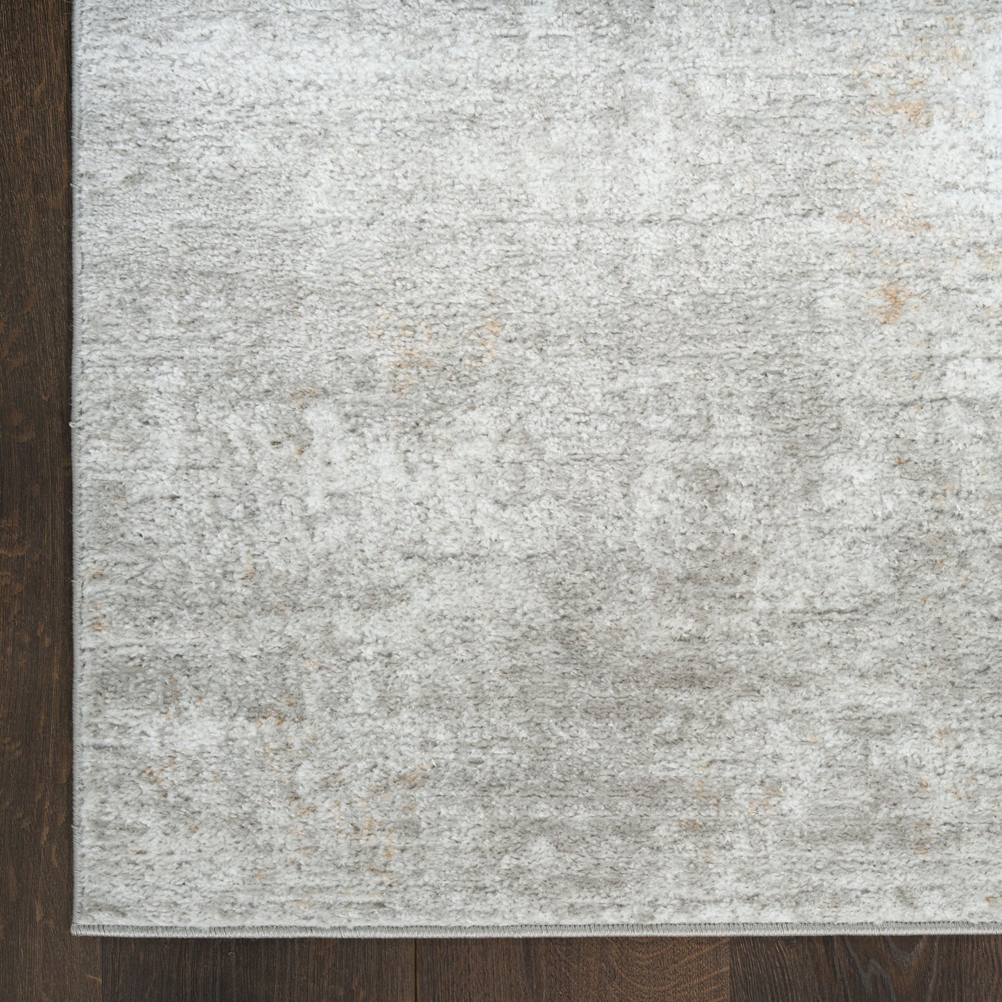 Light gray textured area rug with subtle marbled pattern on dark wood floor, corner view.