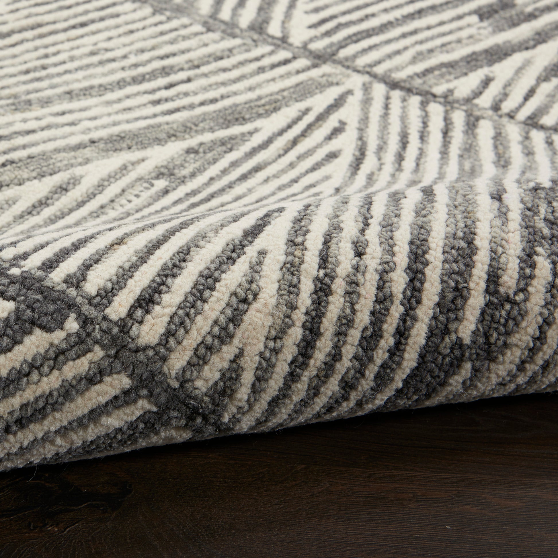 Close-up of a plush rug with grey and cream zebra-like stripes and a textured pile resting on dark wood floor.