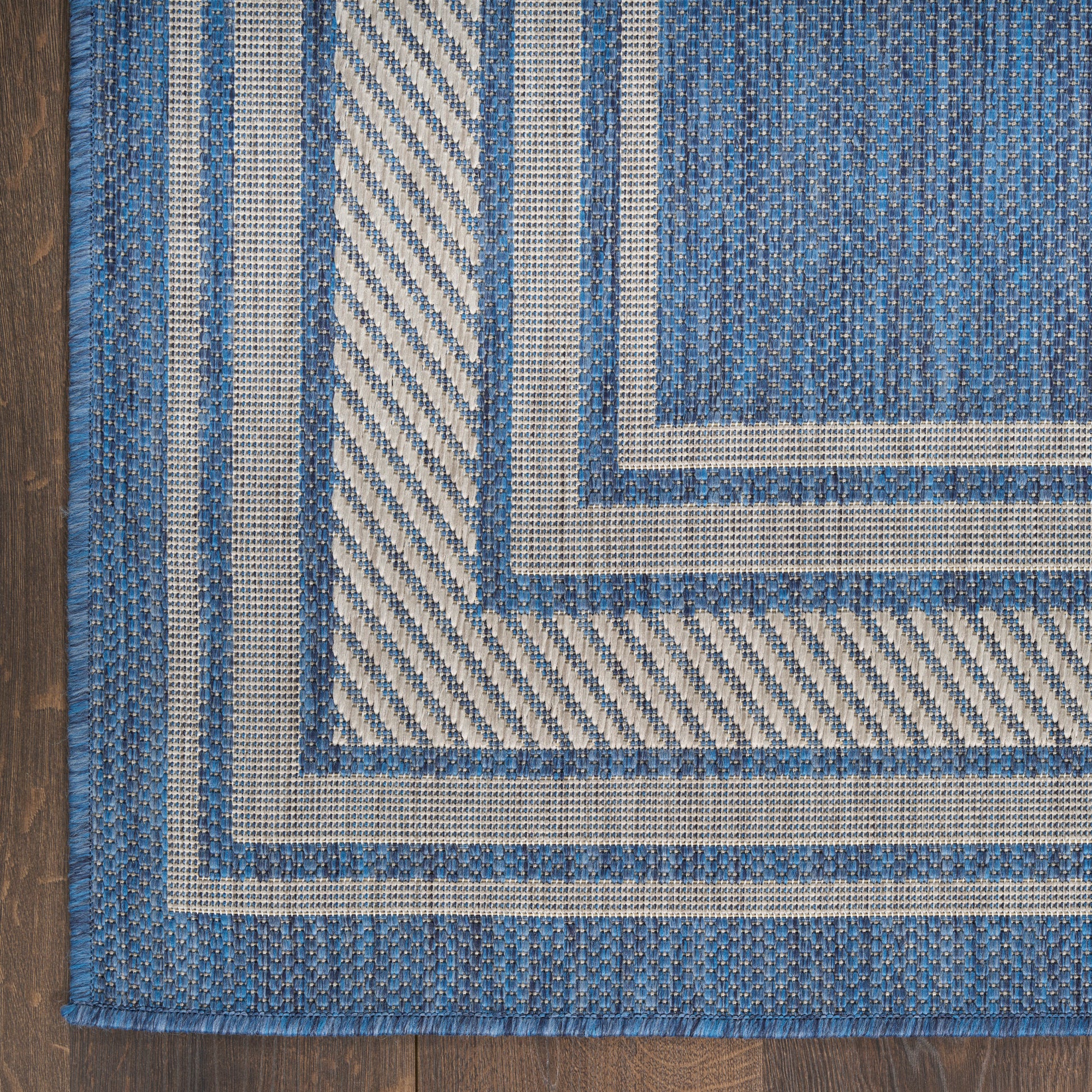 Blue and cream flat-weave rug with concentric borders on a wooden floor, textured weave.