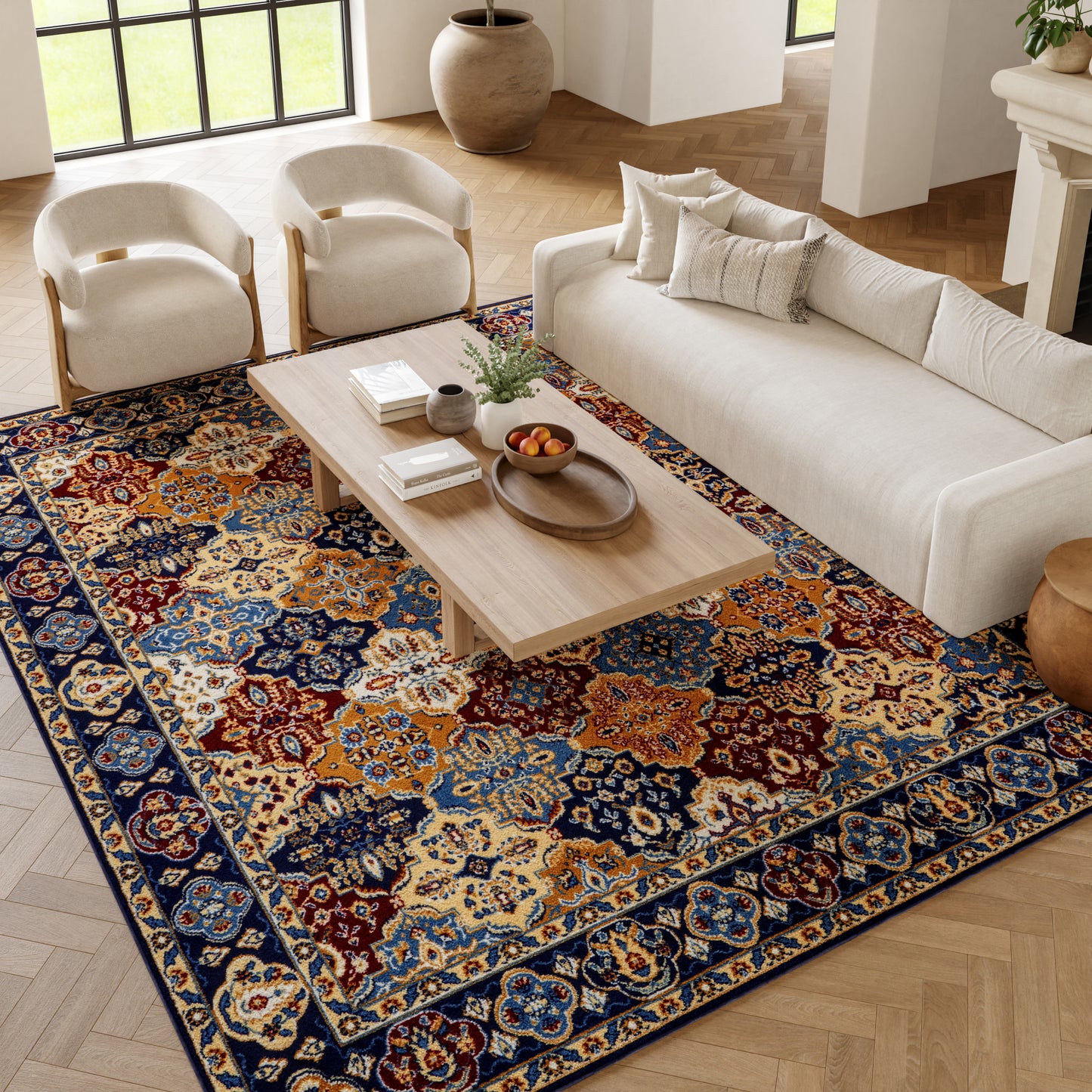 Living room with a large multicolor oriental rug in blue, orange and cream, a light wood coffee table, cream sofa, and beige armchairs.