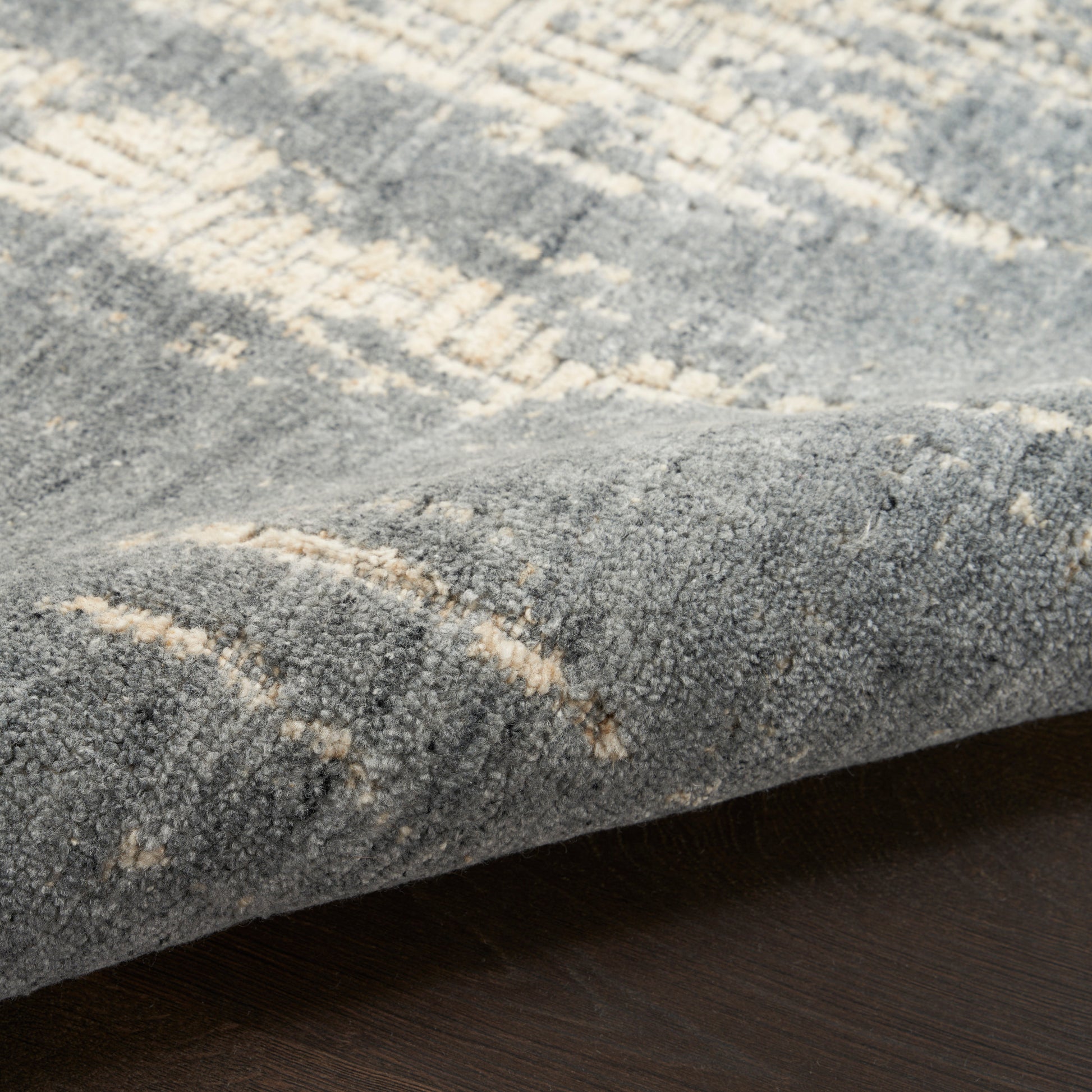 Blue-gray textured area rug with cream abstract pattern, plush pile, edge folded on dark wood floor.