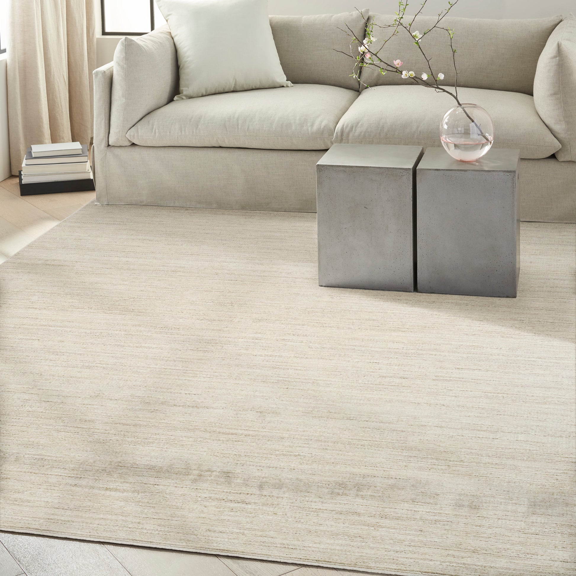 Neutral living room with cream sofa, concrete cube side tables, glass vase with blossoms, and a beige rug.