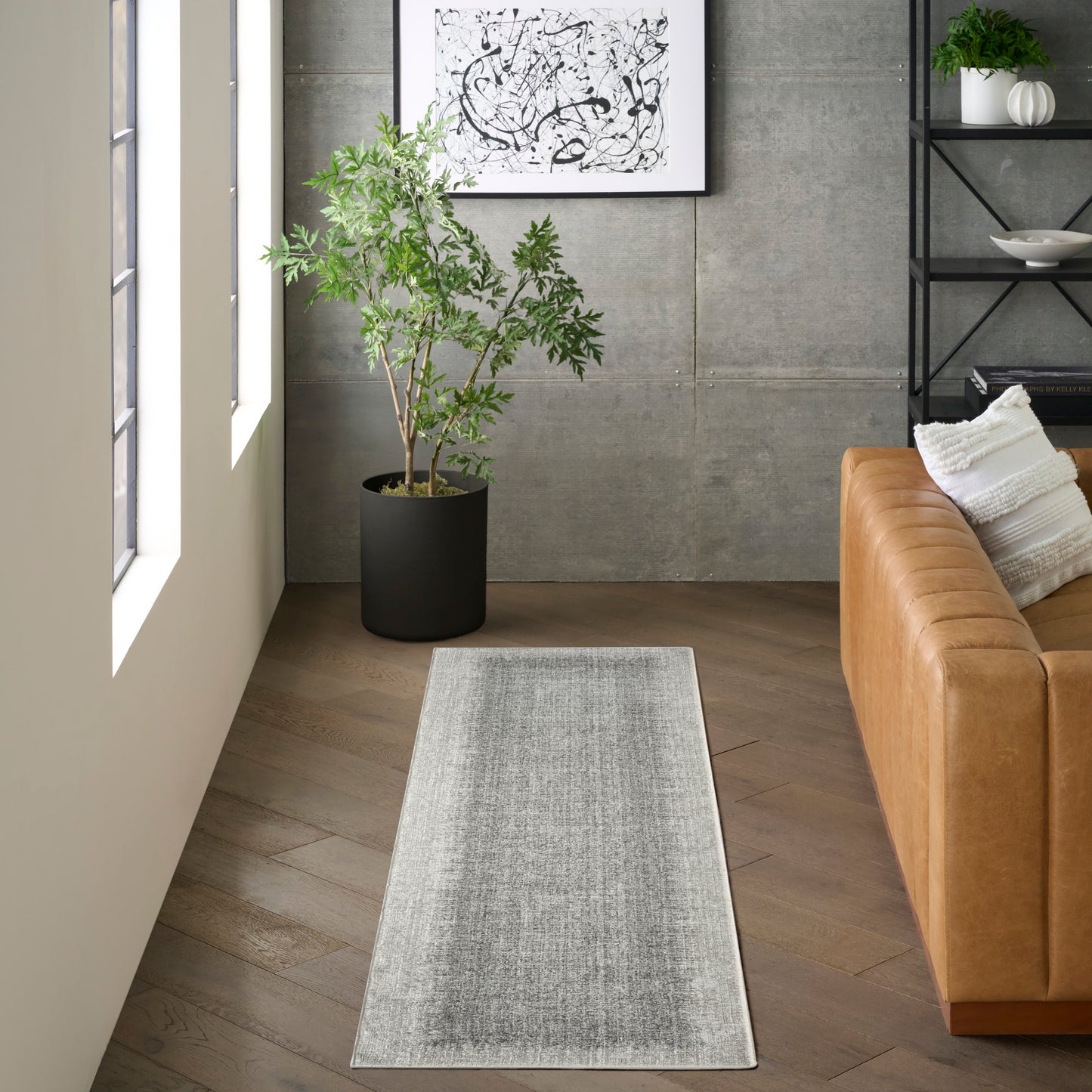 Gray woven runner rug on wood floor beside a tan leather sofa in a modern living room with a potted plant and abstract art.
