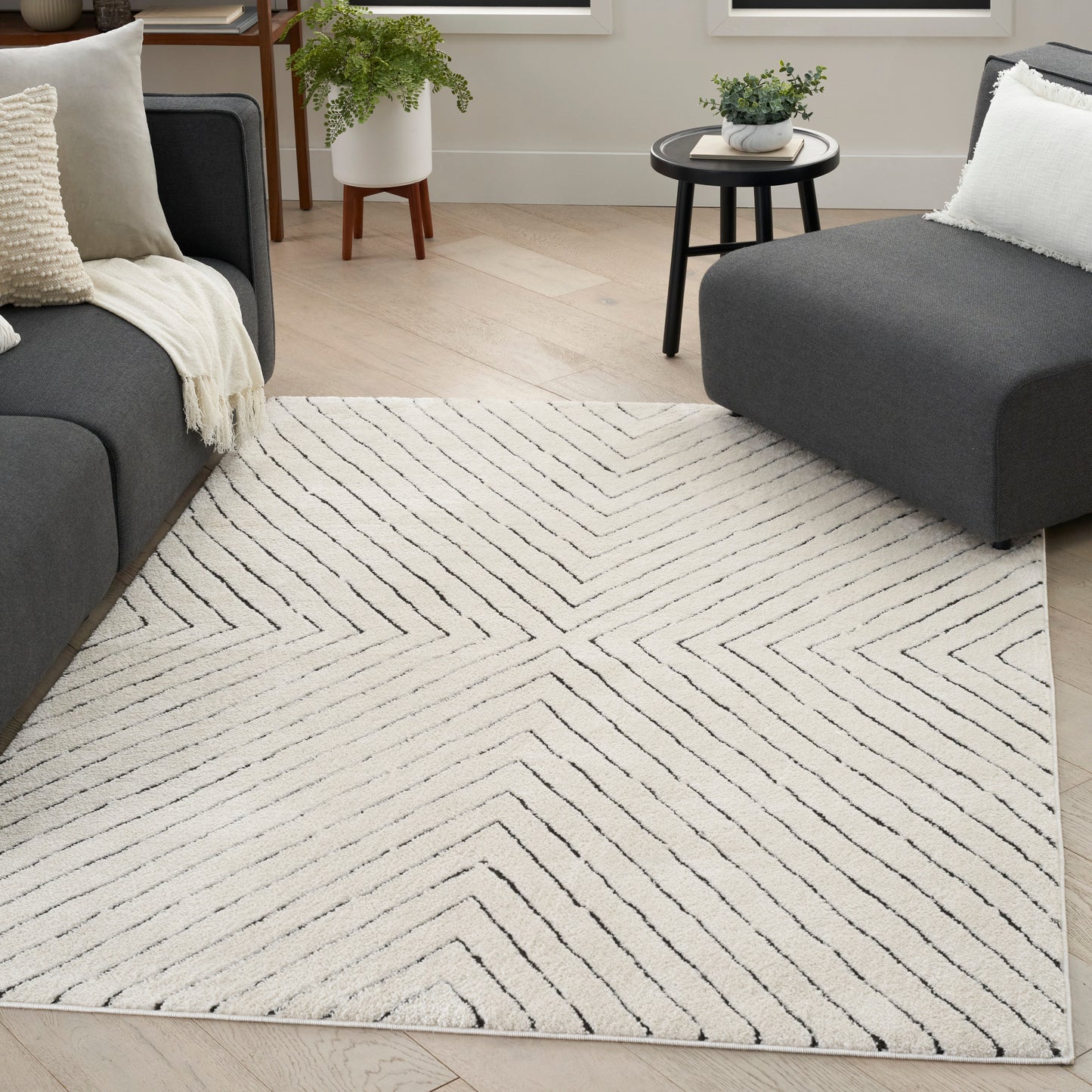 Cream area rug with black chevron lines in a contemporary living room with gray sectionals and light wood flooring.