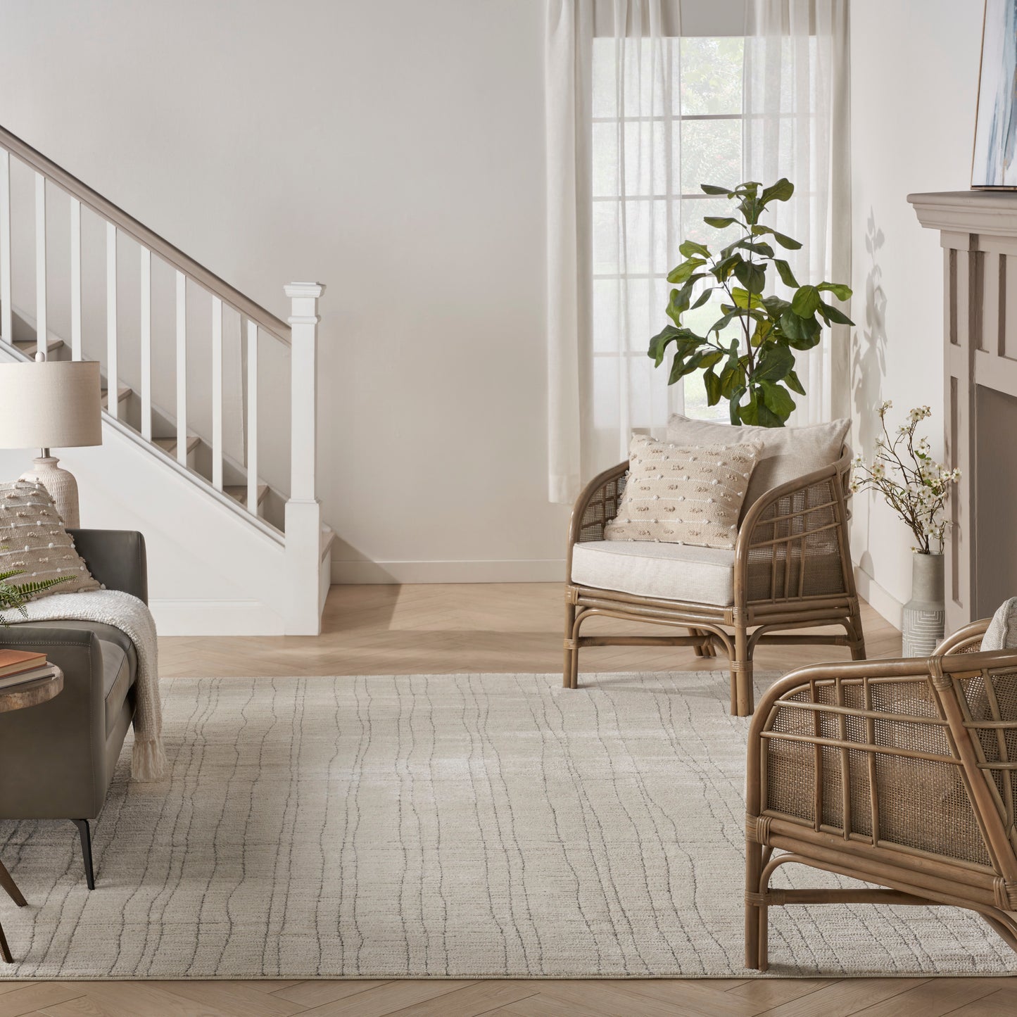 Bright living room with rattan chairs, a neutral woven rug, potted plant, and a white staircase under daylight.
