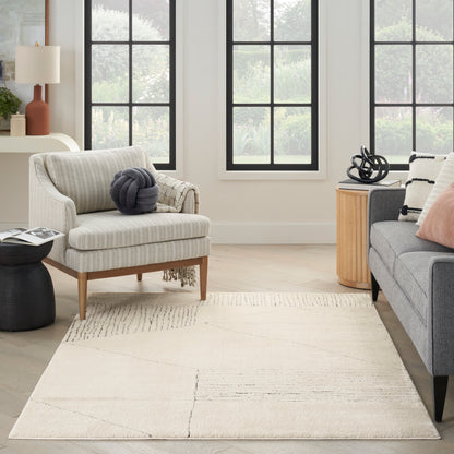 Beige striped armchair with wooden legs and a gray knot pillow beside a gray sofa; cream geometric rug and round wood side table.