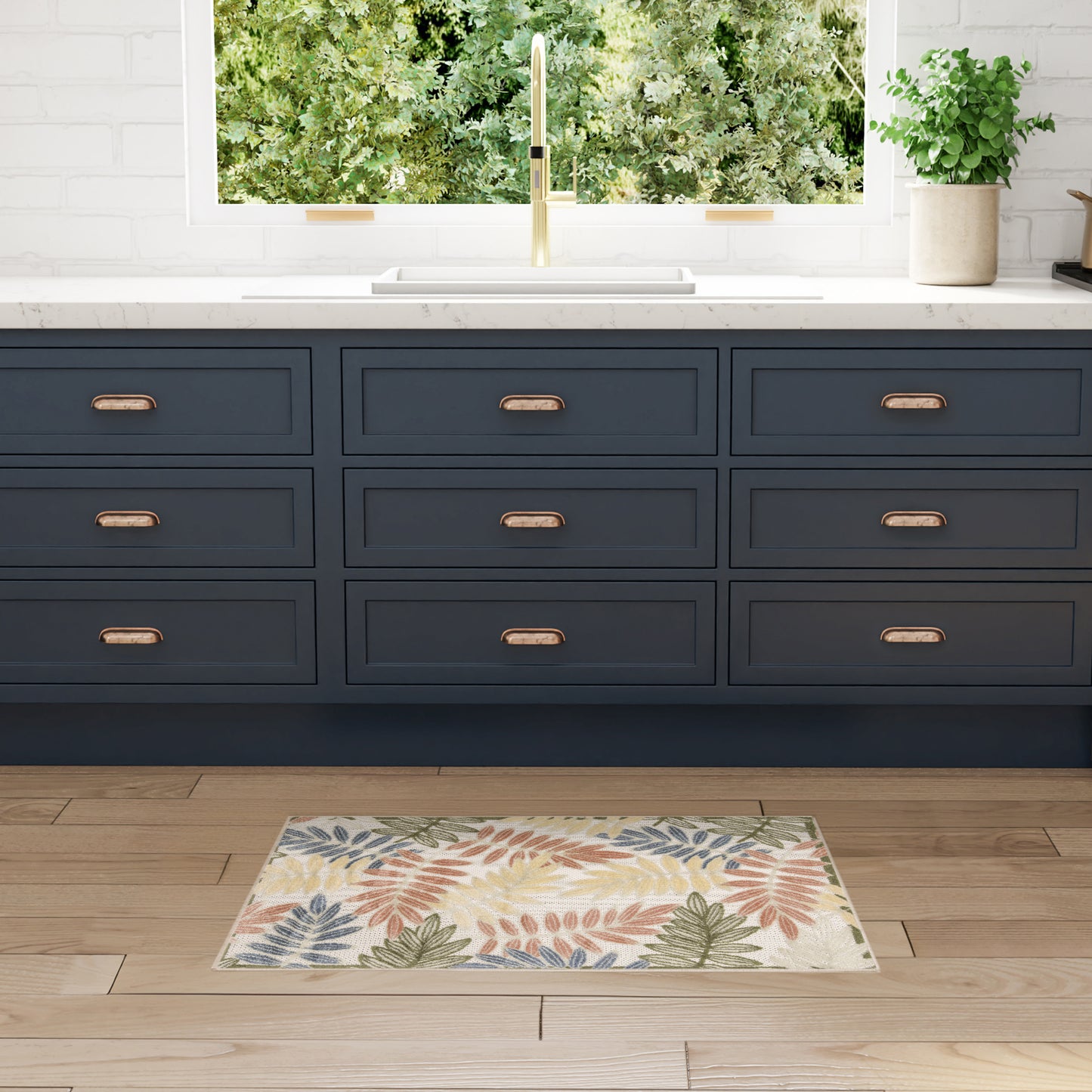 Dark blue kitchen base cabinets with brass handles, white countertop, gold faucet, leafy-pattern rug on wooden floor.