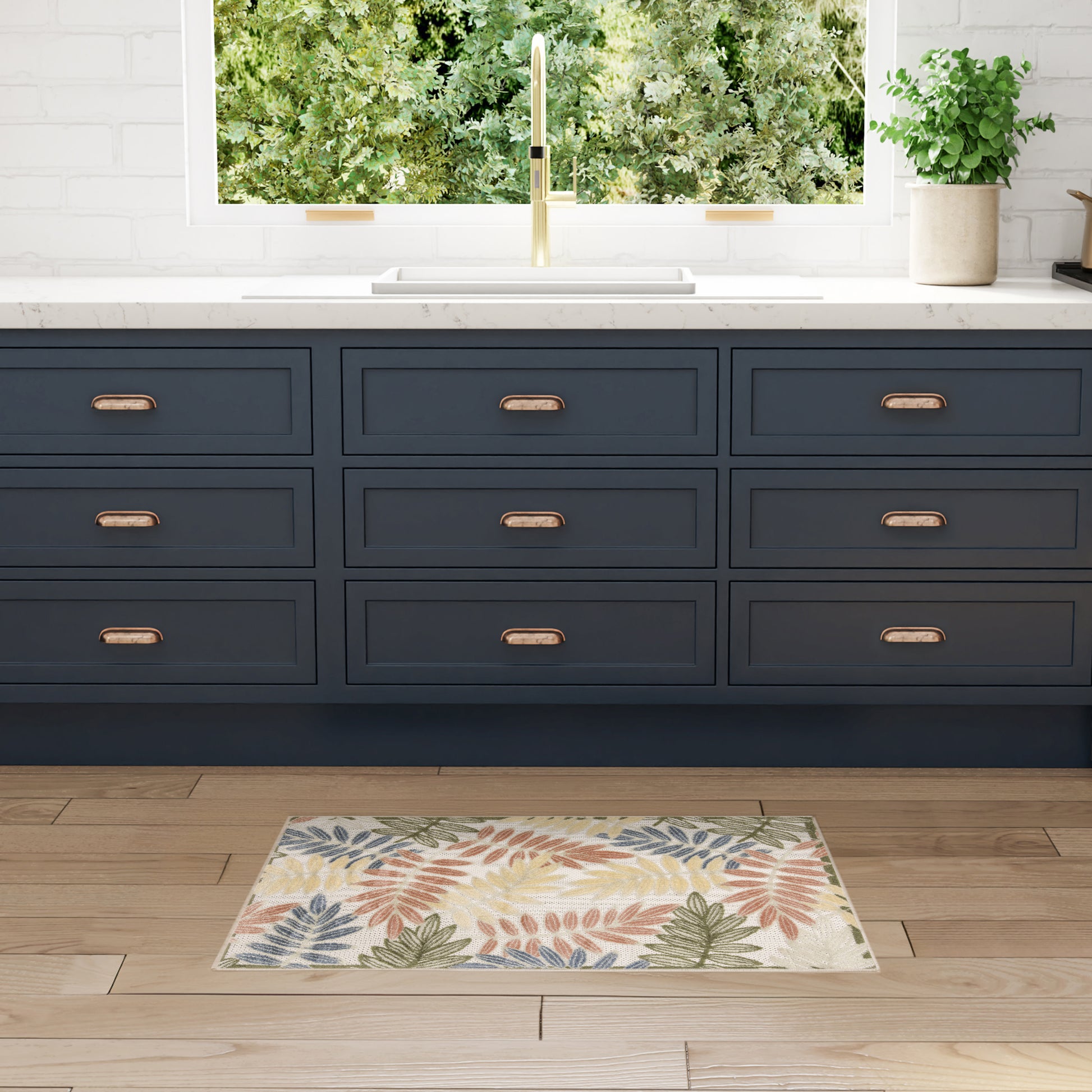 Dark blue kitchen base cabinets with brass handles, white countertop, gold faucet, leafy-pattern rug on wooden floor.