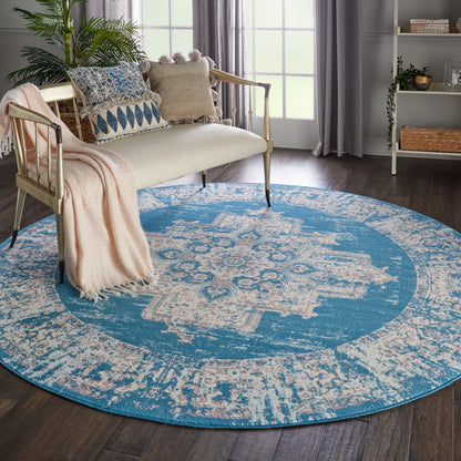 Round blue area rug with ivory distressed geometric pattern in a cozy living room with a beige sofa and plants.