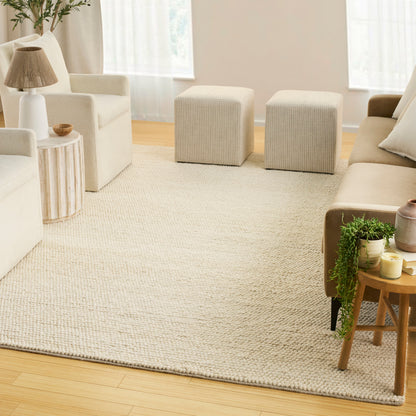 Bright Scandinavian living room with cream sofa, two light gray cube ottomans, textured beige rug, wooden tables and plants.