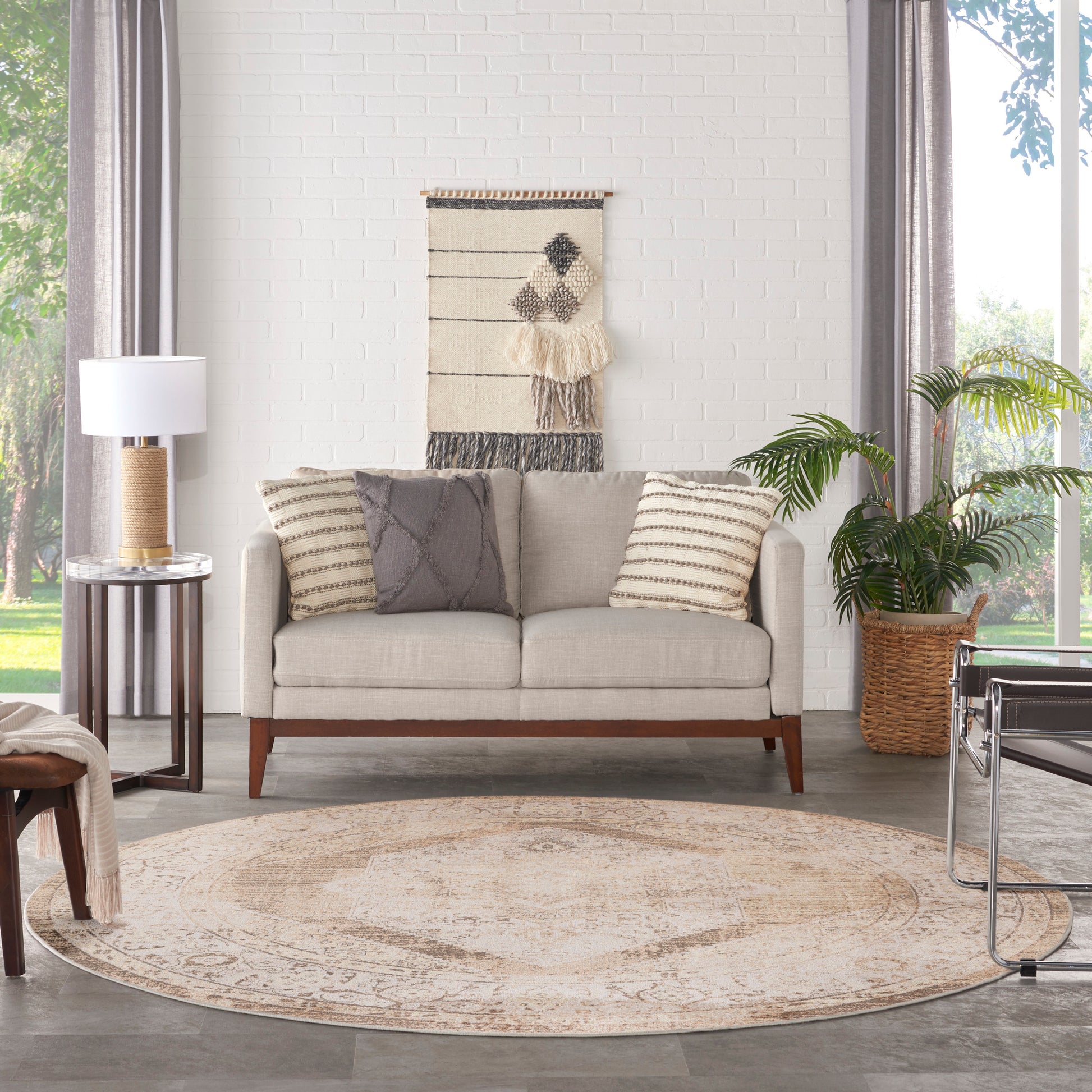Beige sofa with striped and solid cushions, round beige rug, woven wall hanging, potted plant in basket.