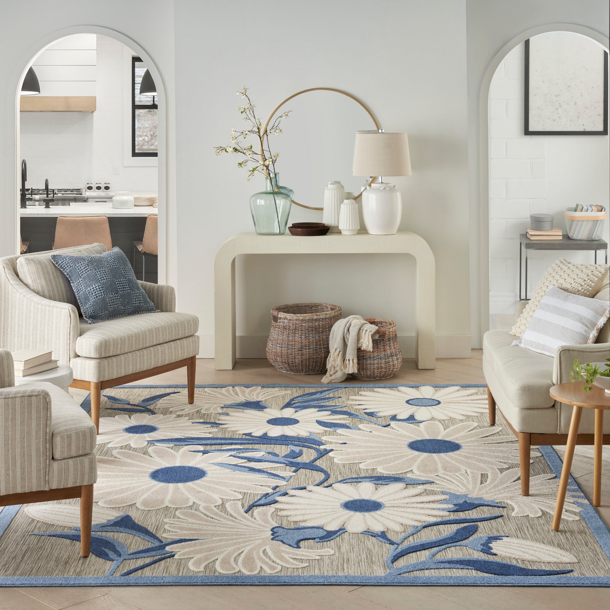 Cream living room with arched doorways, beige upholstery, blue floral area rug, wooden legs, and a curved console with vases.