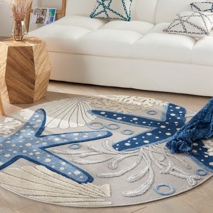 Round coastal rug with blue starfish and seashell patterns on a beige background in a modern white living room.