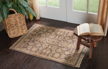 Beige-brown oriental rug with fringe on dark wood floor & wicker plant basket & small wooden stool with open book nearby.