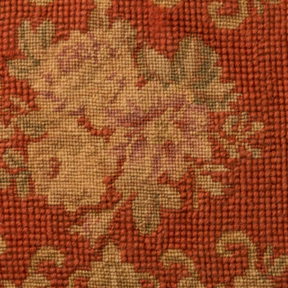 Rust-orange woven rug with beige floral motif; textured tapestry fabric.
