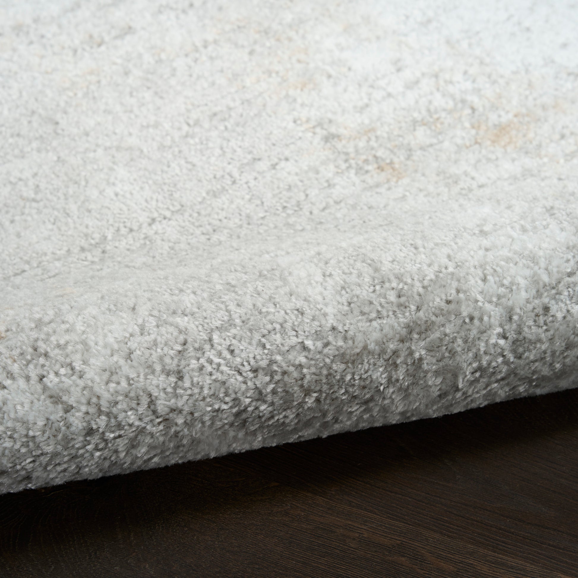 Light gray shag rug with dense plush pile, soft and cozy, folded edge over dark wood floor.