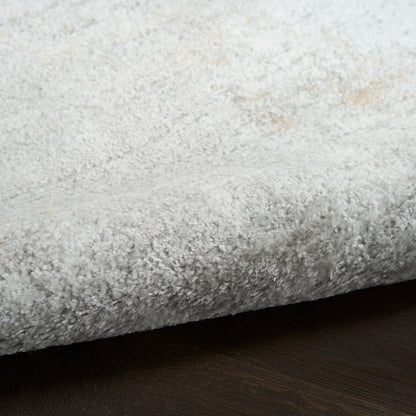 Light gray shag rug with dense plush pile, soft and cozy, folded edge over dark wood floor.