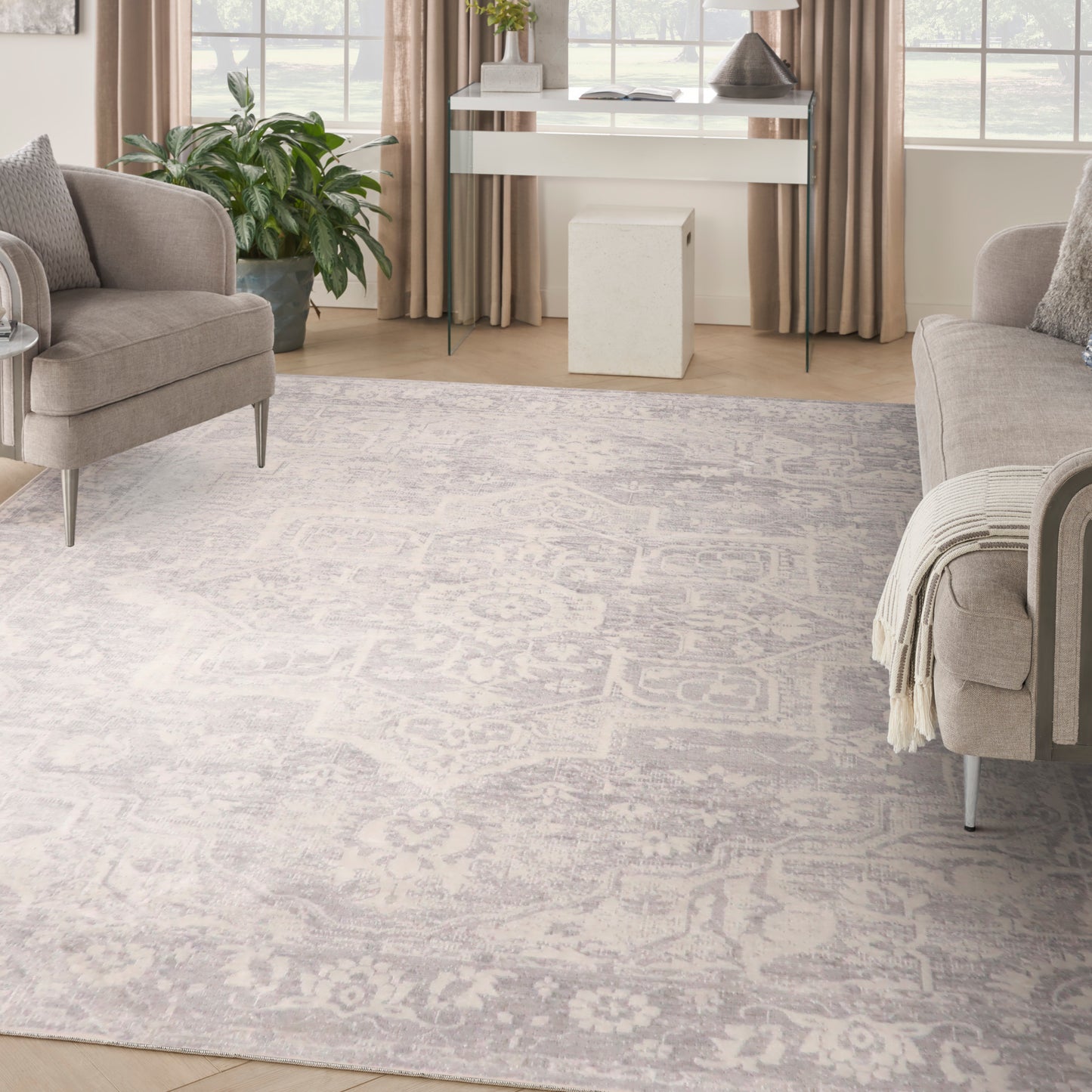 Soft gray patterned area rug anchors a contemporary living room with taupe sofas, beige curtains, glass console table, and a green plant.