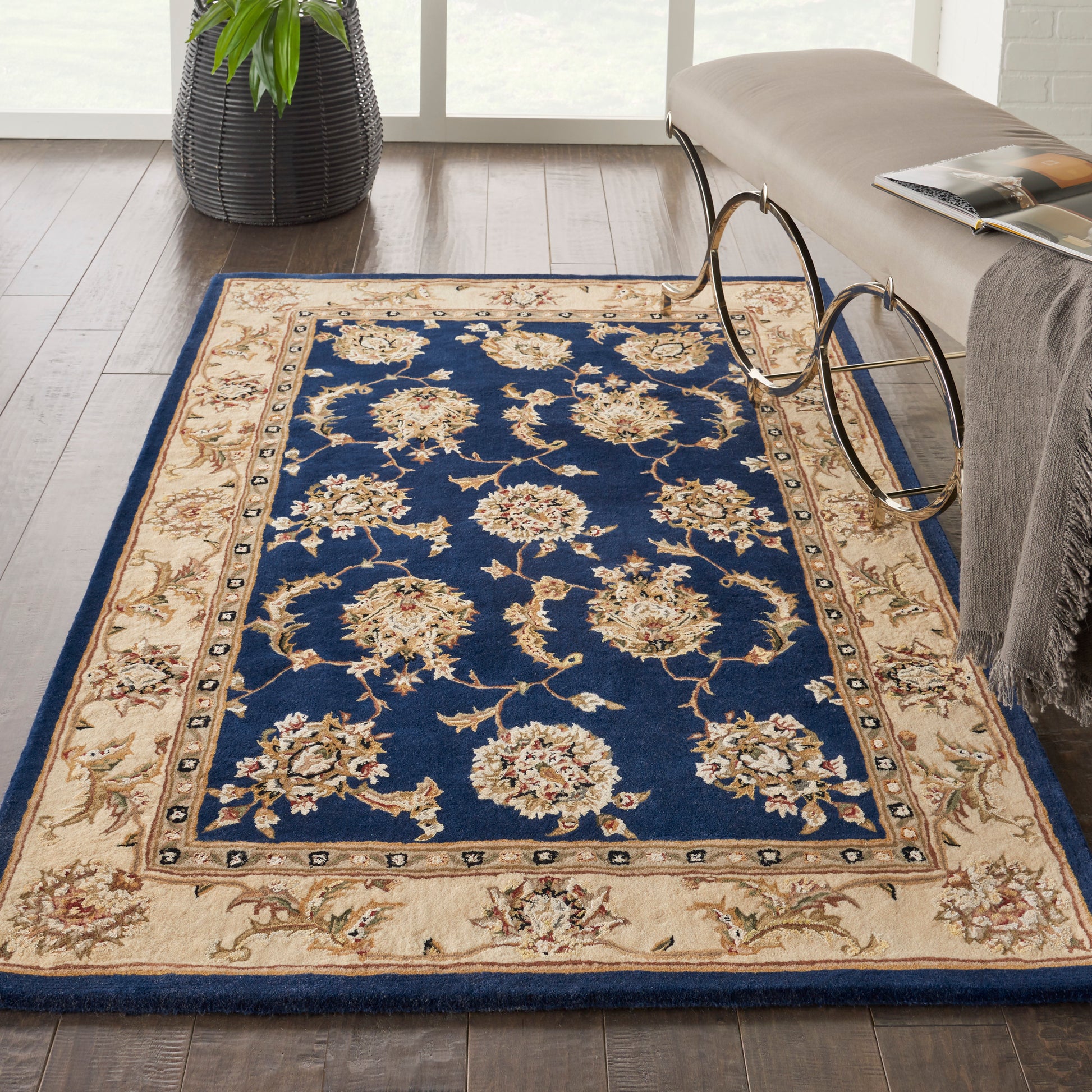 Rectangular rug with navy blue center and cream floral borders; beige border with scrolling vines on a wood floor.