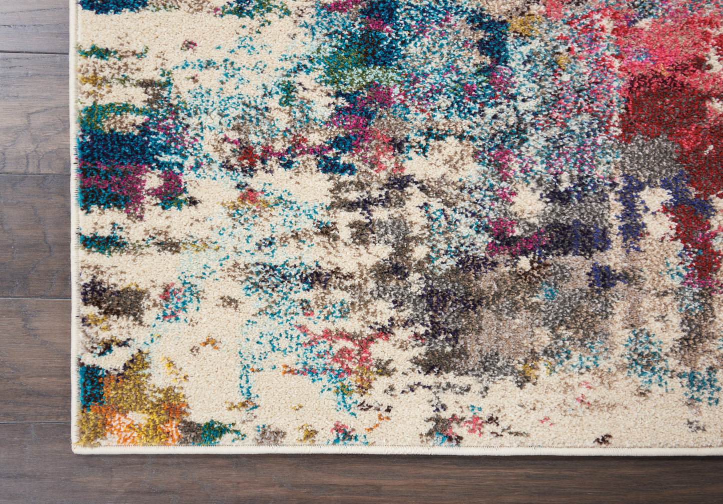 Abstract area rug with cream base and bright blue, teal, pink, and gray splashes on a wooden floor.