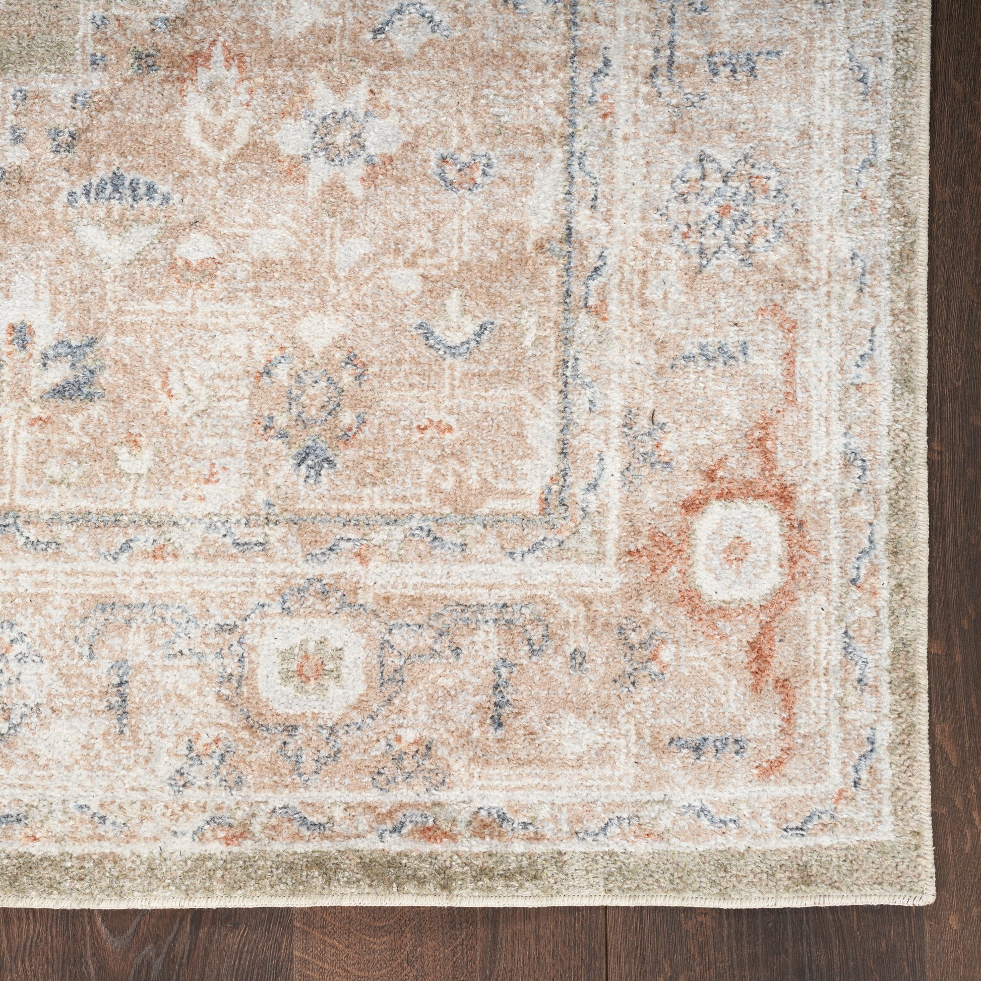 Vintage-inspired peach-beige rug with blue floral pattern and pale border on wood floor.