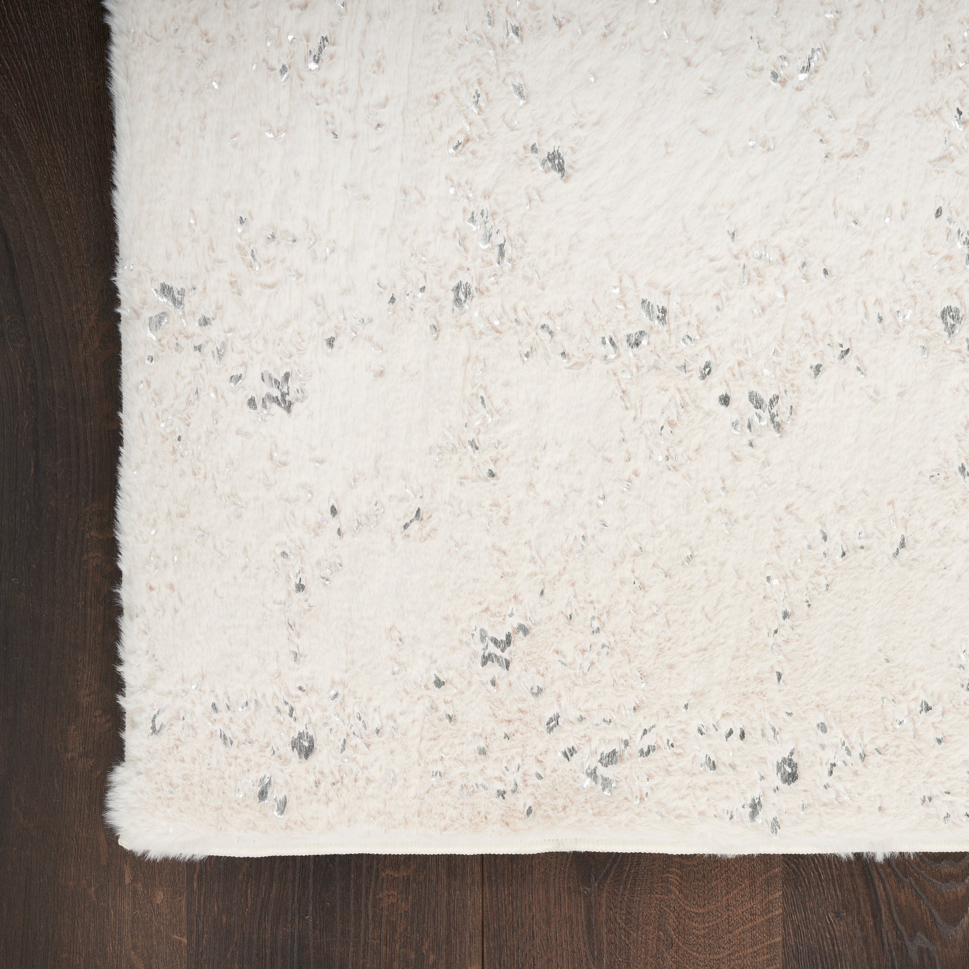 Cream shag rug with silver-gray flecks on dark wood floor; soft, fluffy rectangular rug.