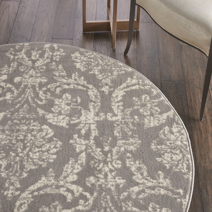 Round gray rug with ivory damask floral pattern on dark wood floor; beige upholstered chair legs visible.